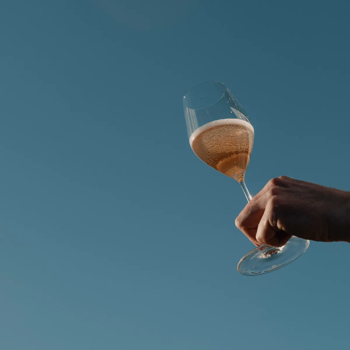 Hand hält ein Glas Rosé-Sekt vor blauem Himmel