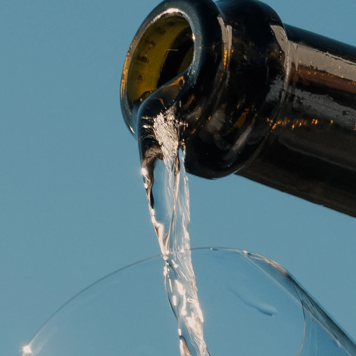Sekt wird vor blauem Himmel aus der Flasche ins Glas gegossen